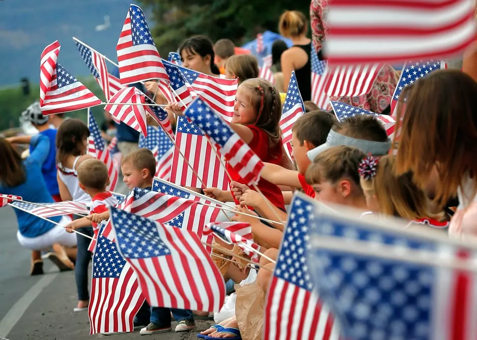 Children and adults gathered outdoors, waving American flags, likely during a patriotic celebration or parade.