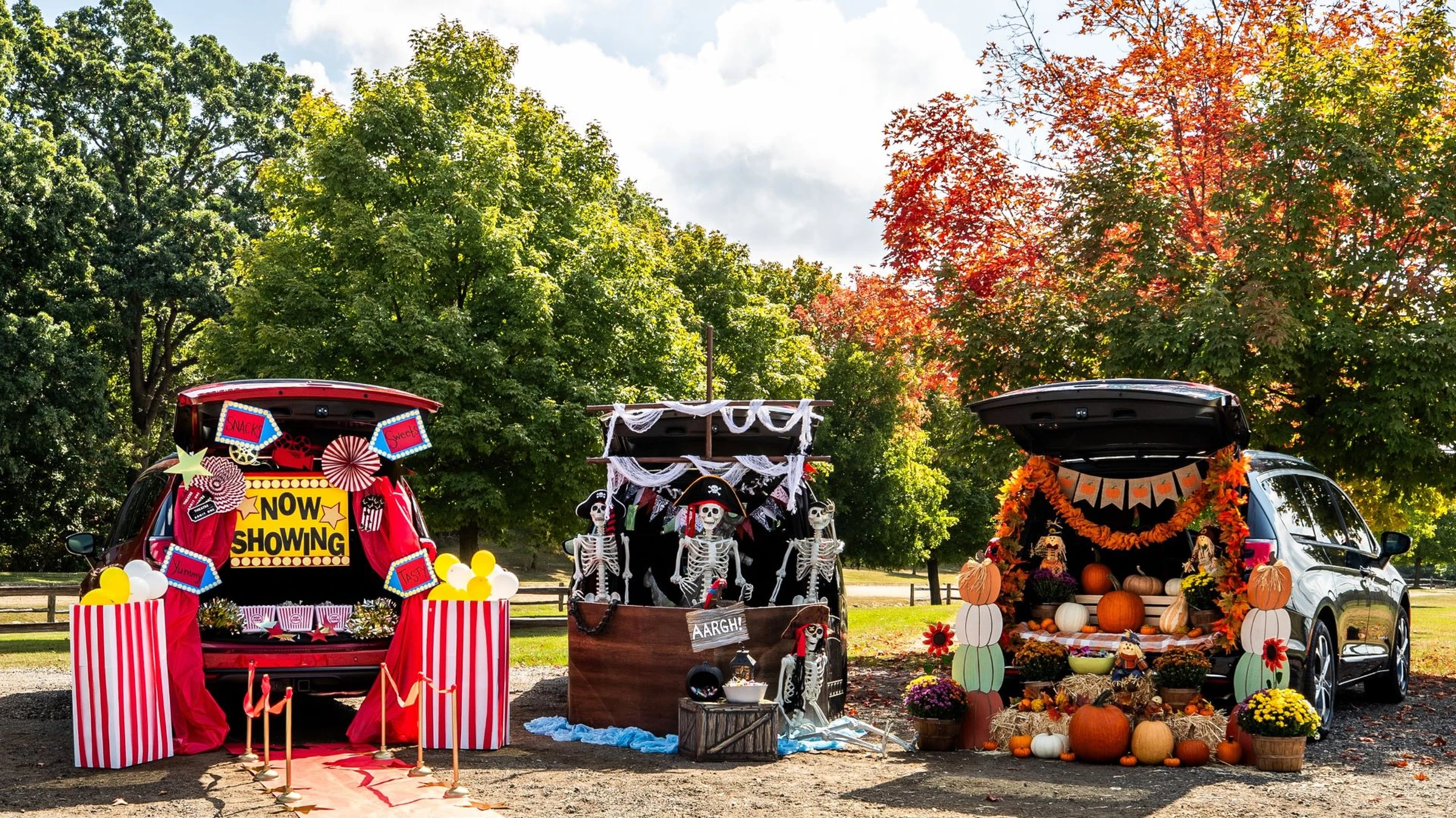 Three decorated car trunks: one like a theater, one with skeletons, and one with pumpkins and fall decor, all set outdoors on a sunny autumn day.