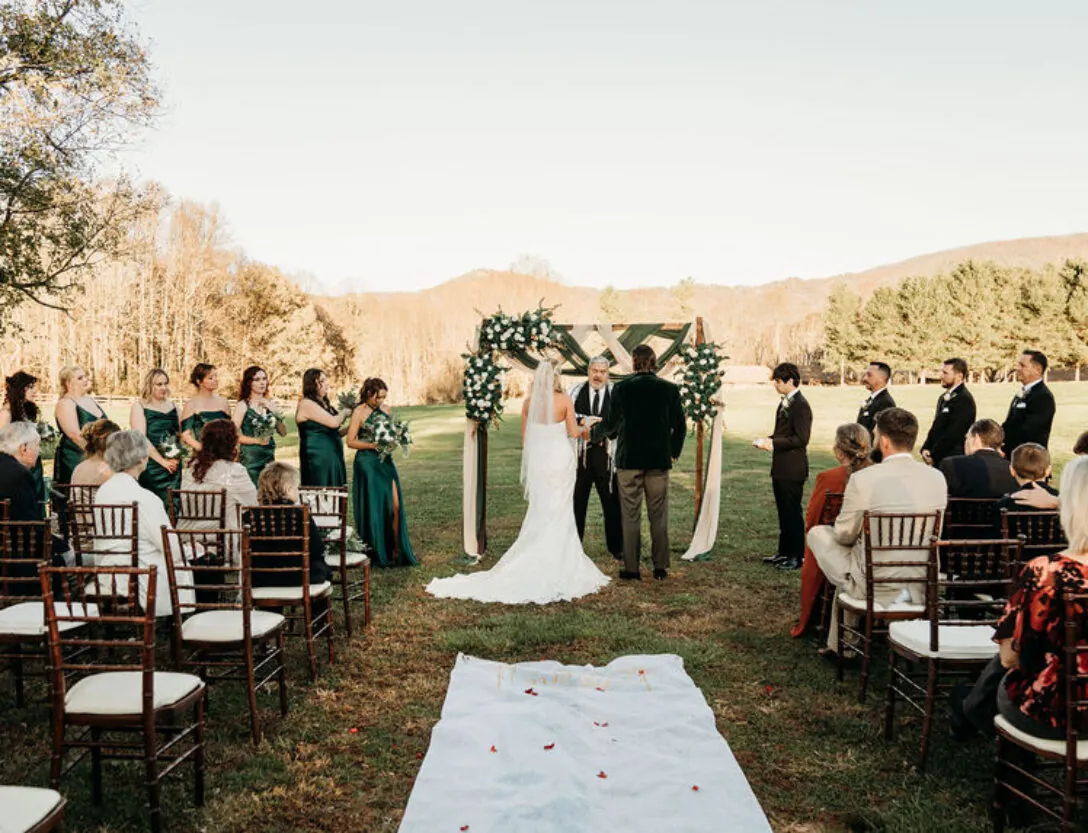 Outdoor wedding ceremony with a bride and groom at the altar, guests seated on both sides, and bridesmaids in green dresses standing to the left.