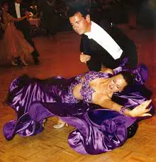 A couple ballroom dancing; the woman in a flowing purple dress leans dramatically as her partner supports her on a polished dance floor.