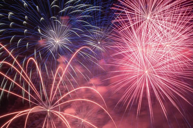 Colorful fireworks bursting in the night sky, displaying vibrant red, pink, blue, and white streaks and patterns.