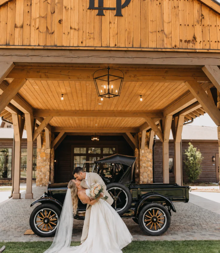 A bride and groom kiss in front of a vintage car at Dillard House PA, under a pavilion—perfect for weddings near hotels in downtown.