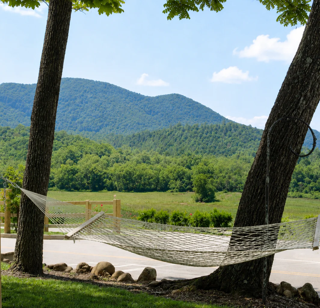 A hammock between two trees overlooks green mountains and a road, near hotels in downtown Dillard House PA under a blue sky.