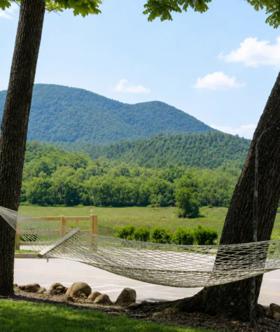 A hammock between two trees overlooks green mountains and a road, near hotels in downtown Dillard House PA under a blue sky.