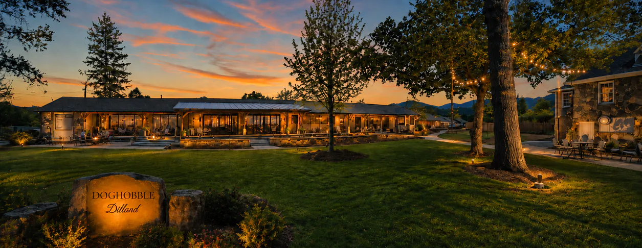 A lodge at sunset with string lights, a stone sign reading Doghobble Dillard, and mountains in the background. Outdoor seating is visible.
