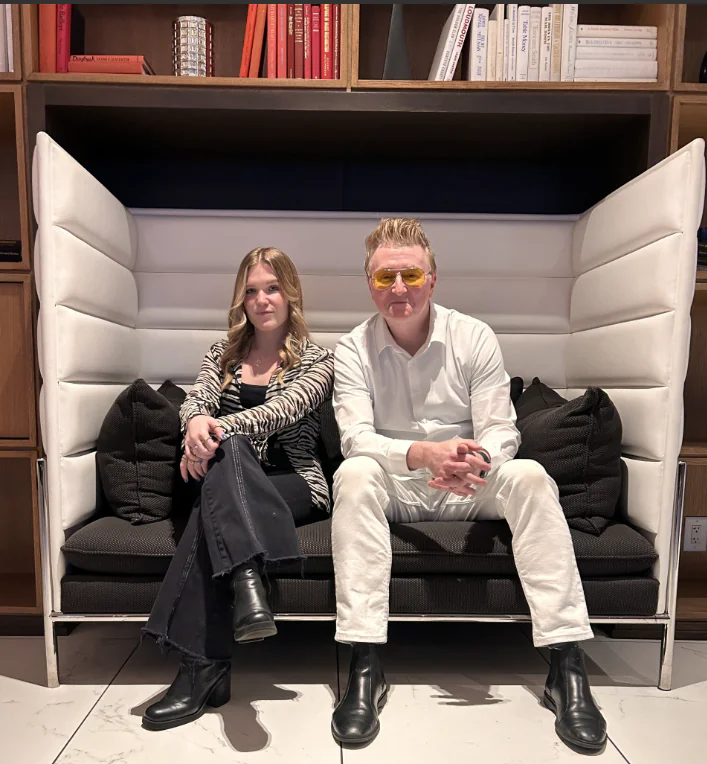 A woman and a man wearing yellow-tinted glasses sit together on a modern black and white booth sofa.
